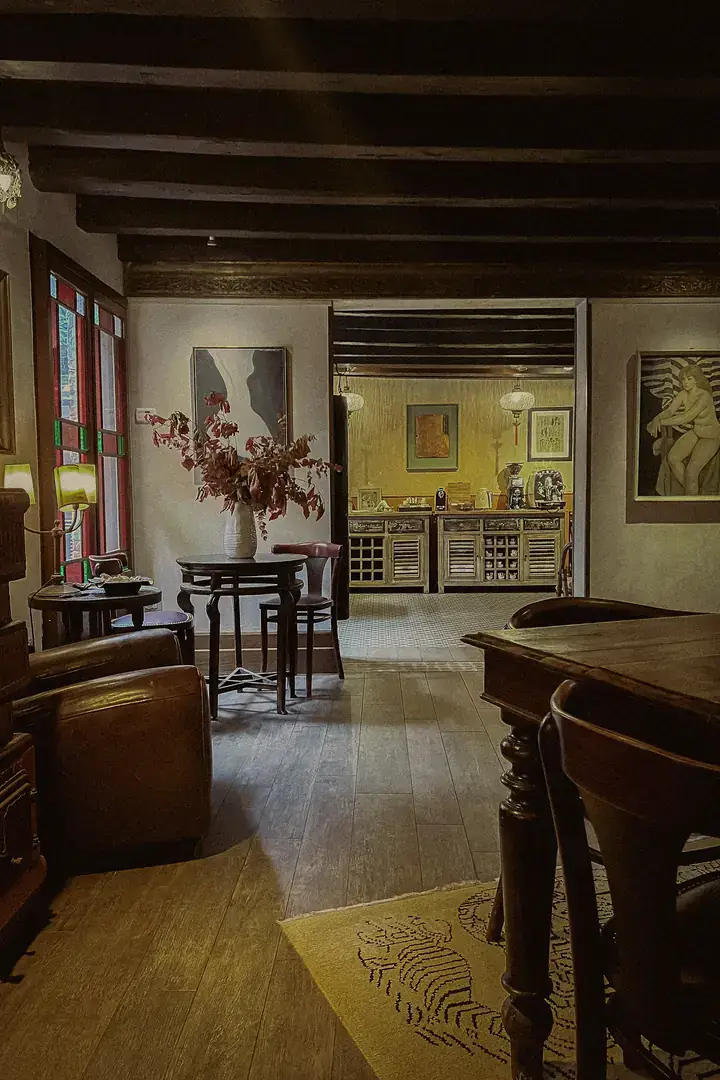 The ground-floor lounge at Novecento, with a leather armchair, small round tables and a vase of autumn foliage, opening onto the breakfast room