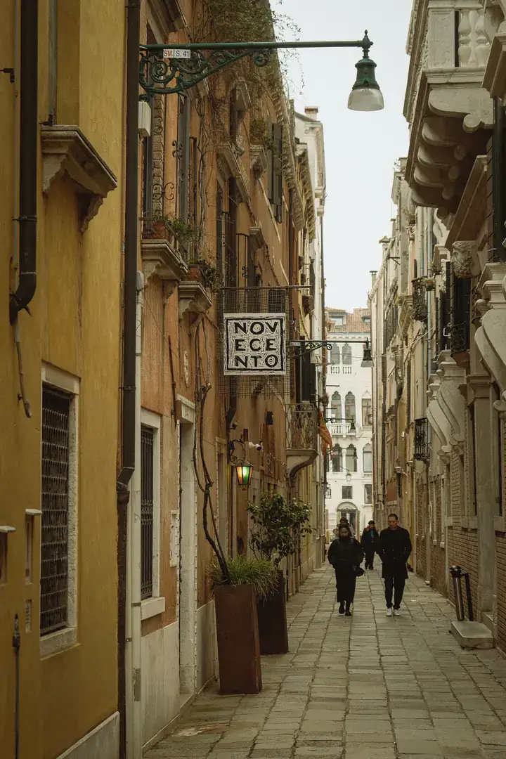 The hanging Novecento sign above a narrow calle in San Marco, lined with ochre buildings and an iron street lamp