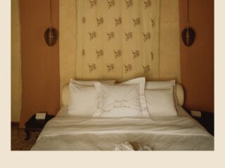A double bed beneath a pierced brass lantern and a printed hanging at Novecento in Venice, with ochre walls and an embroidered pillow